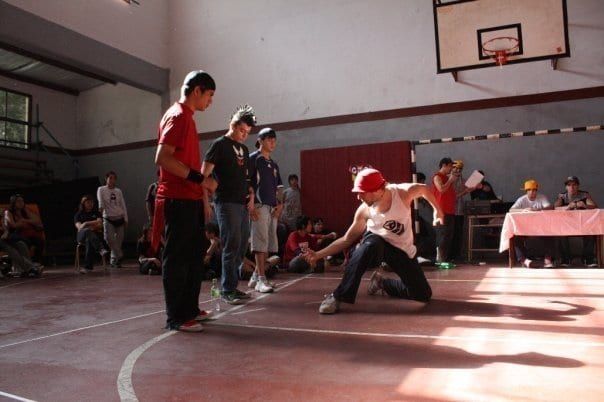 A cypher forming on a school basketball court, one dancer down in a freeze inside the circle