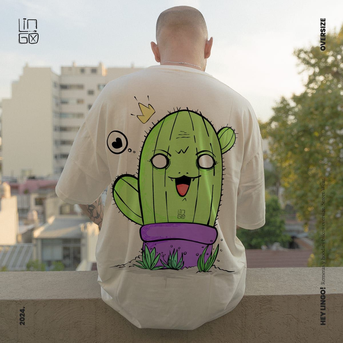 The back of a cream oversize t-shirt printed with a smiling cactus character, worn on a balcony
