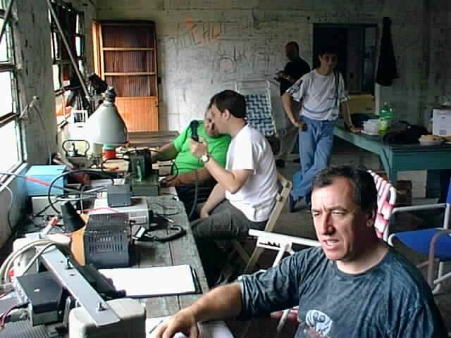 A workbench crowded with radio equipment, test instruments and cabling, a man working at it with more operators behind him